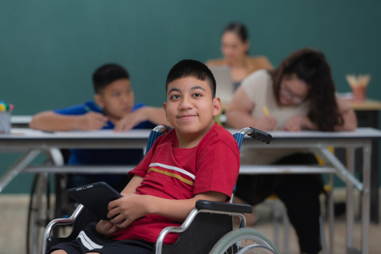 Portrait of young handicapped kid boy sitting on wheelchair and looking to camera with happiness eyes.