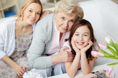 Portrait of happy little girl, her mother and grandmother looking at camera at home