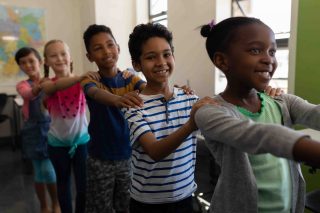 Side view of school kids standing in row with their hands on