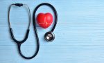 Red heart with stethoscope on blue wooden background - representing healthcare
