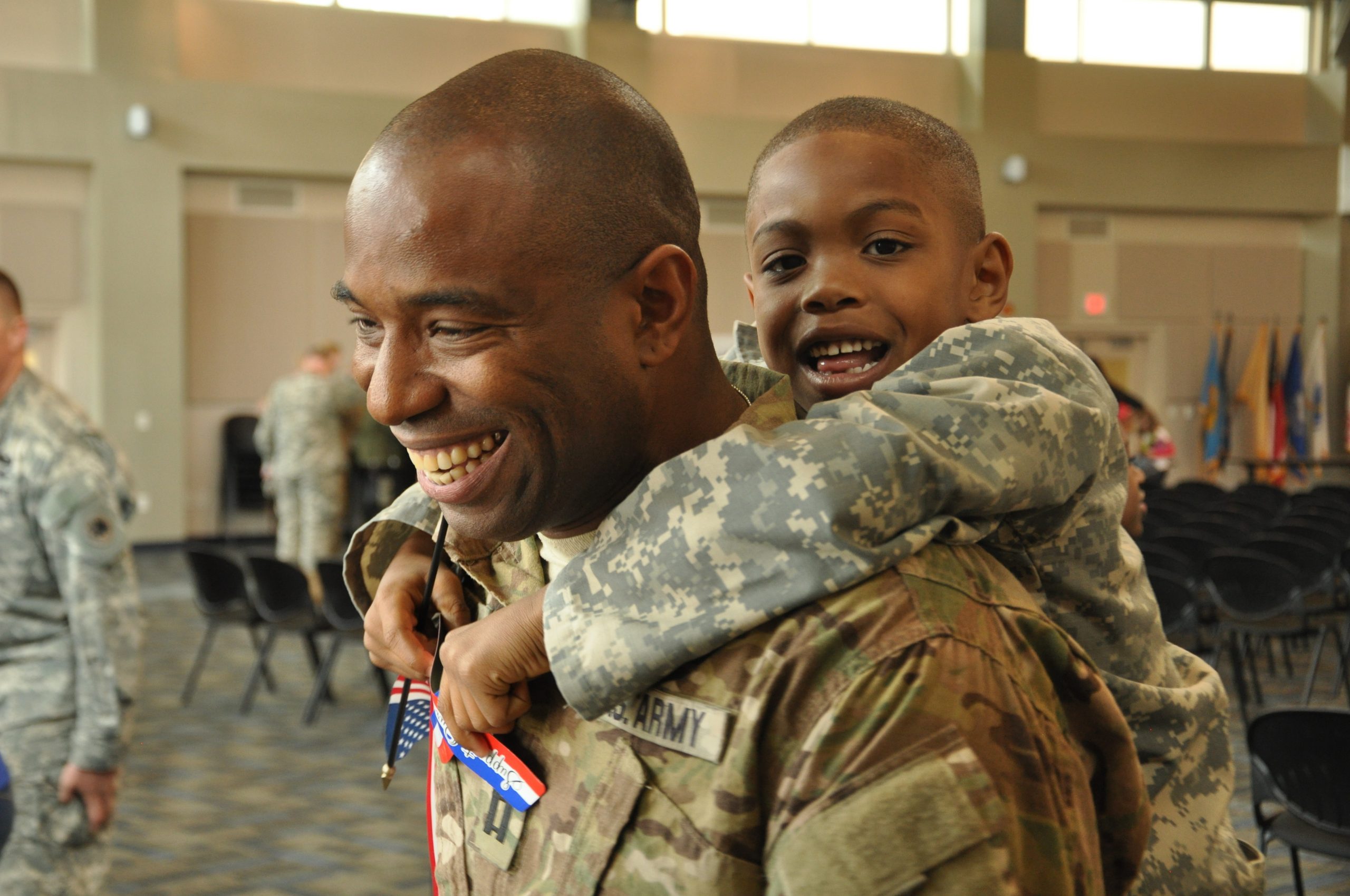 Male service member carrying a young boy piggyback, both smiling