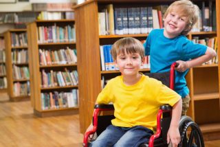 Two smiling boys at the library one is a wheelchair