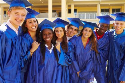 A group of diverse youth pose for in their cap and gown for a graduation photo