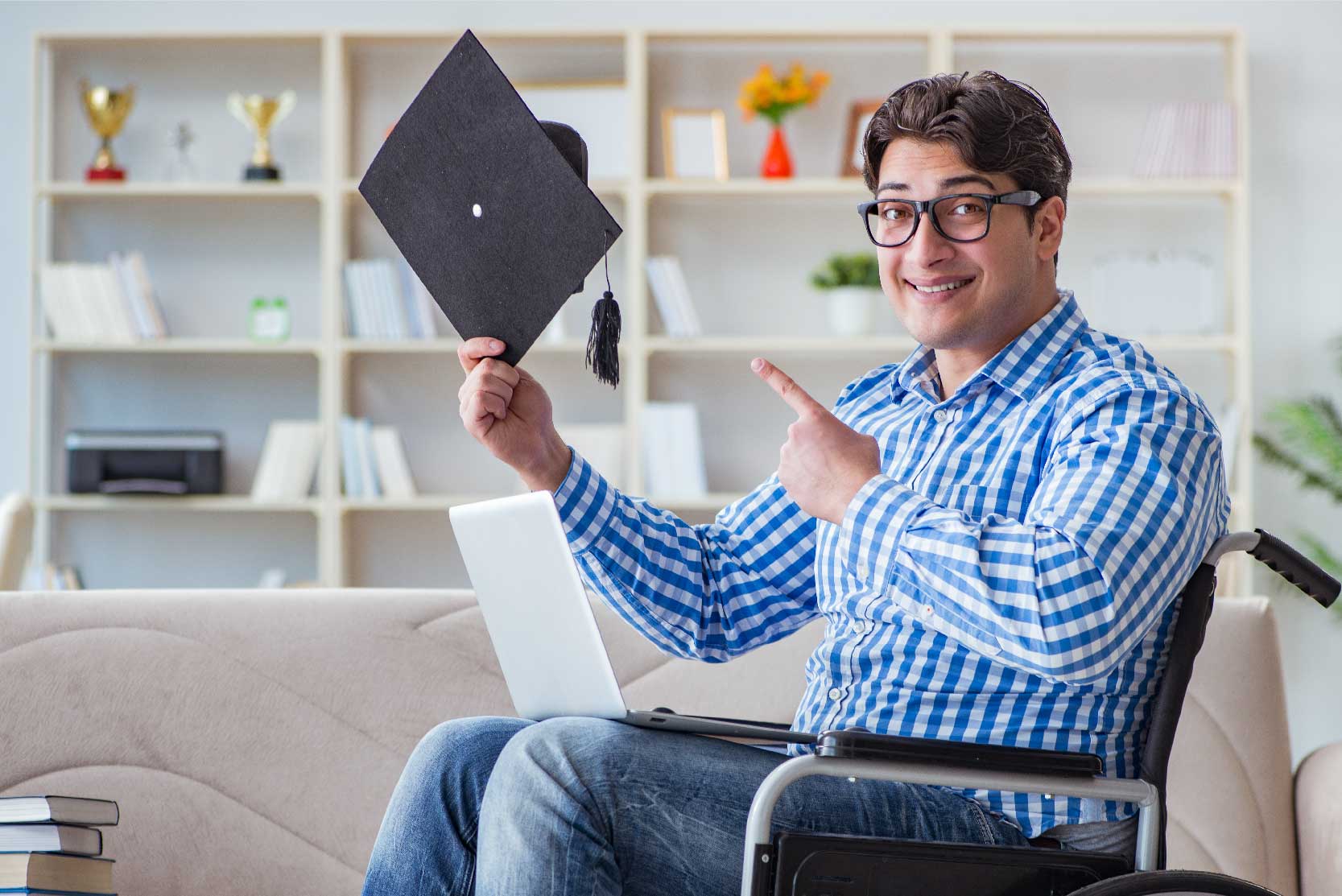 Young man in a wheelchair smiles and points to a graduation cap