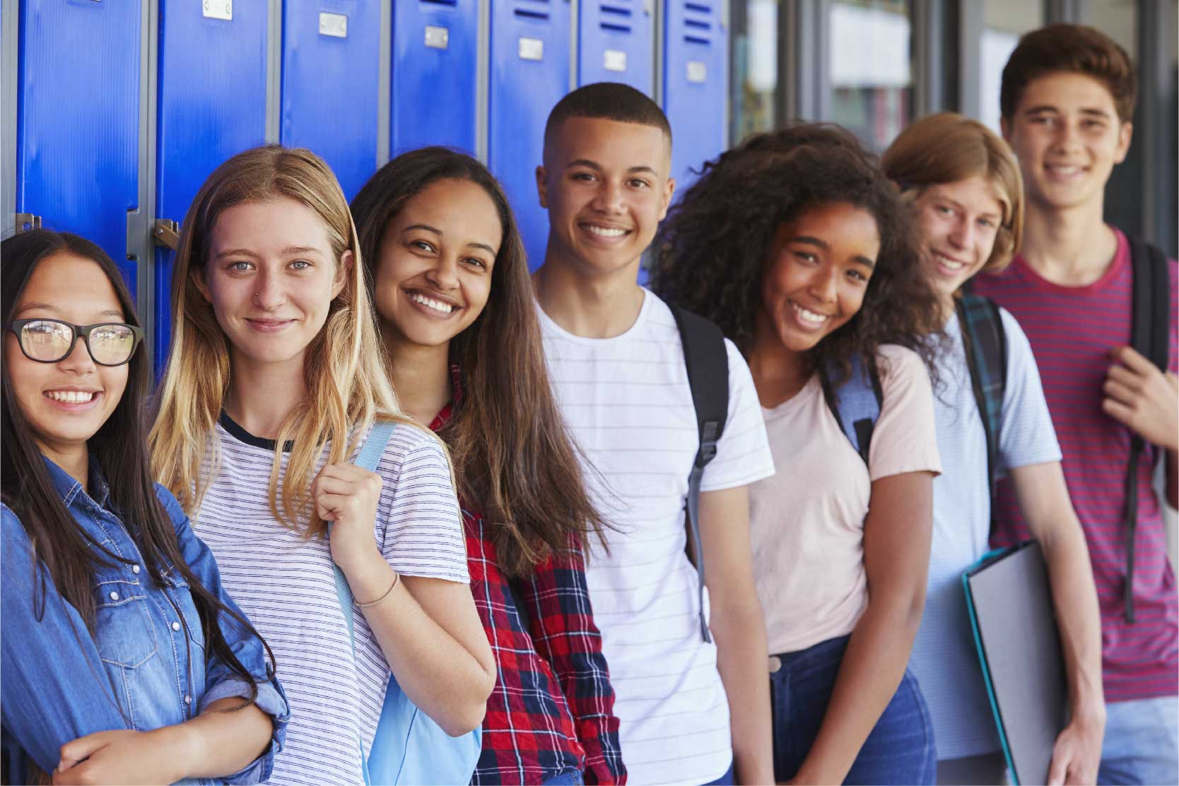 A group of diverse teens pose and smile in front of blue lockers