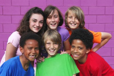 A happy group of diverse kids pose in front of a purple wall