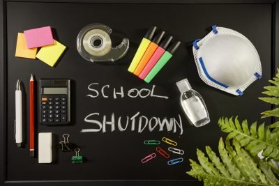 Caronavirus school shutdown concept with personal mask, hand sanitizer and stationery on black flat lay, school shutdown written with chalk on black board, overhead view