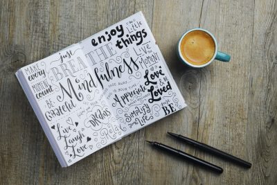 MINDFULNESS hand-lettered sketch notes in notepad on wooden desk with cup of coffee and pens