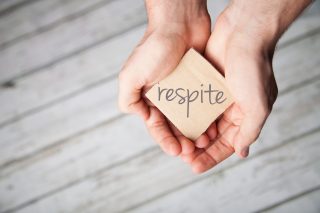 The word Respite is held from two kind hands
