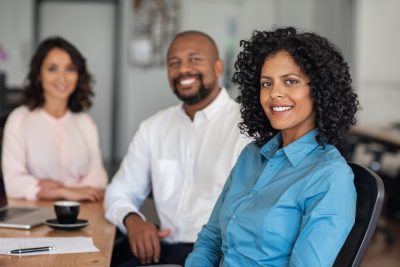 Portrait of a smiling businesswoman sitting with diverse colleagues at a table in an office before a meeting