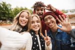 Group of cheerful multiethnic friends teenagers spending fun time together outdoors, taking a selfie