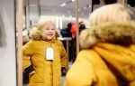 Cute little boy trying new coat during shopping. Fashion warm clothes for fall or winter. Kid/child in fitting room or in shopping center/mall
