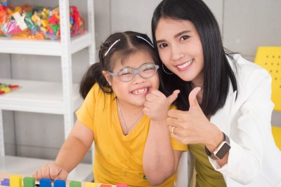 Portraits of a beautiful Asian teacher and a cute girl with autism doing an activity in a class A disabled child thumbs up and smiles to look at the camera.