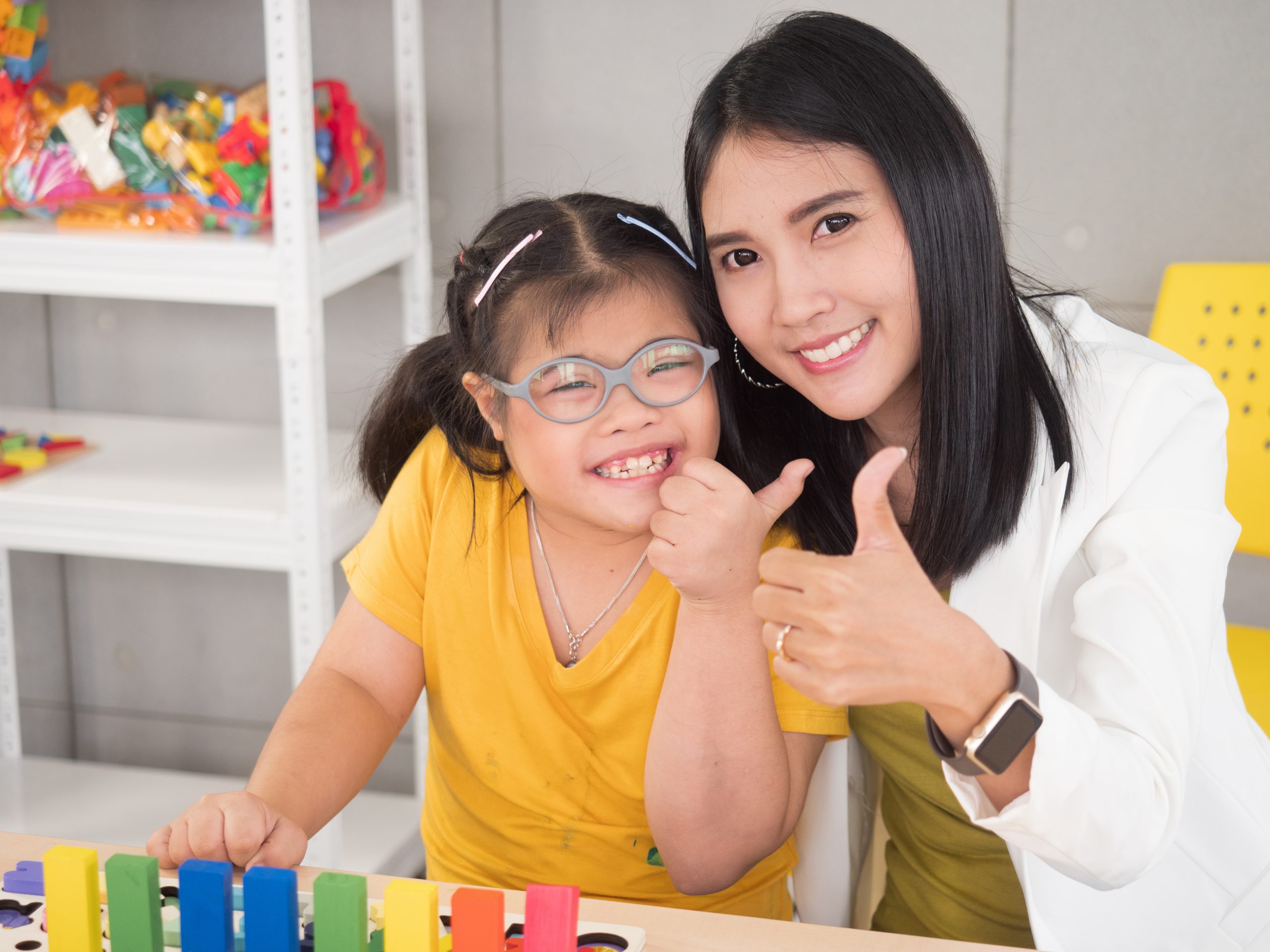 Portraits of a beautiful Asian teacher and a cute girl with autism doing an activity in a class A disabled child thumbs up and smiles to look at the camera.