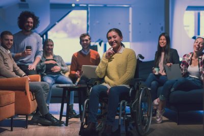 Portrait of businesswoman wheelchair user in front of her diverse business team in a modern open space coworking office space.