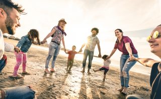 Happy multiracial families round dancing at the beach on ring around the rosy style - Multicultural happiness joy concept with mixed race people having fun outdoor at sunset