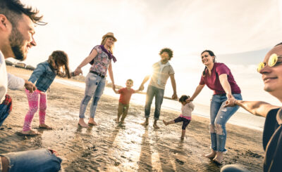 Happy multiracial families round dancing at the beach on ring around the rosy style - Multicultural happiness joy concept with mixed race people having fun outdoor at sunset