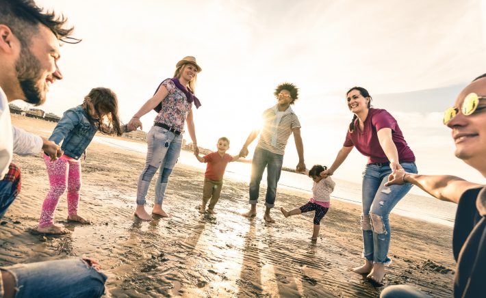 Happy multiracial families round dancing at the beach on ring around the rosy style - Multicultural happiness joy concept with mixed race people having fun outdoor at sunset