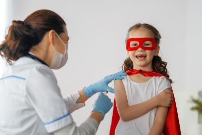Doctor vaccinating child at hospital. Kid in superhero costume.