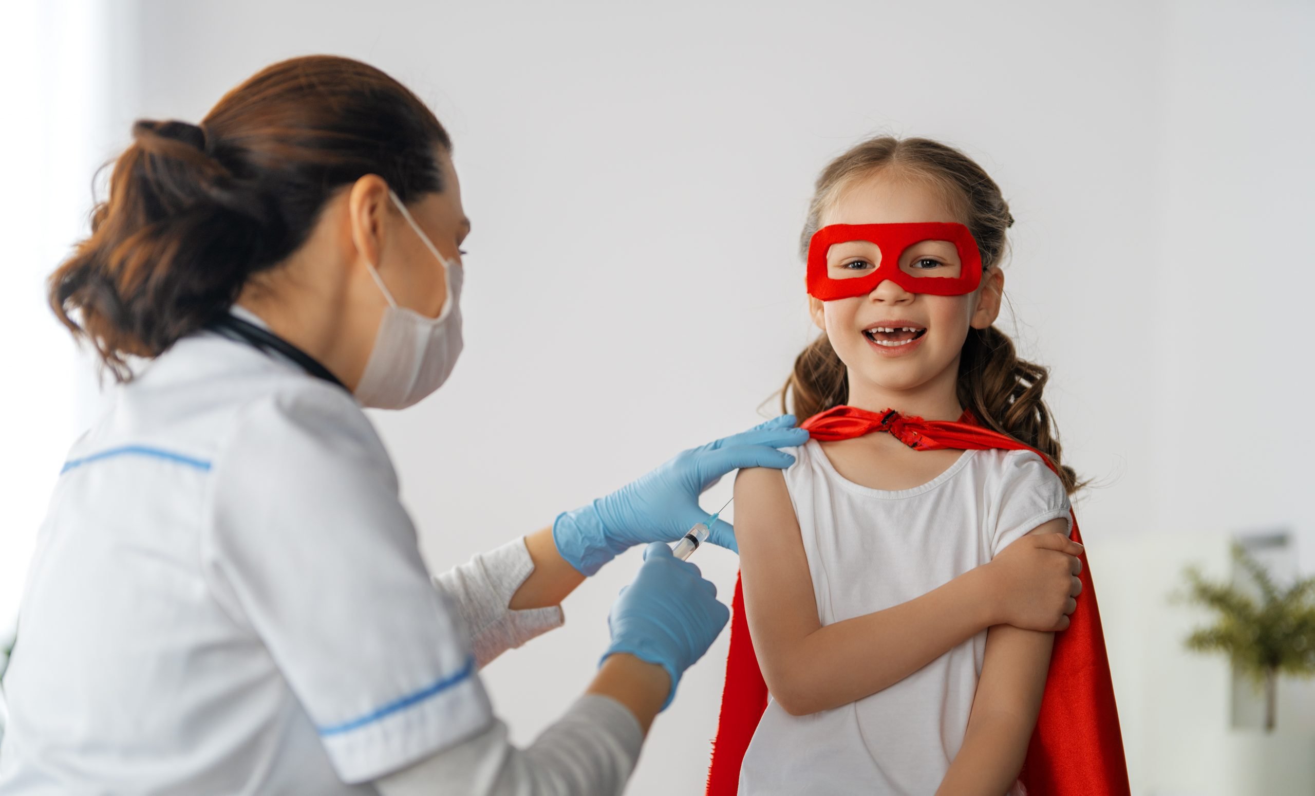 Doctor vaccinating child at hospital. Kid in superhero costume.