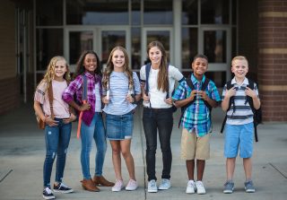 Large Group portrait of pre-adolescent school kids smiling in front of school