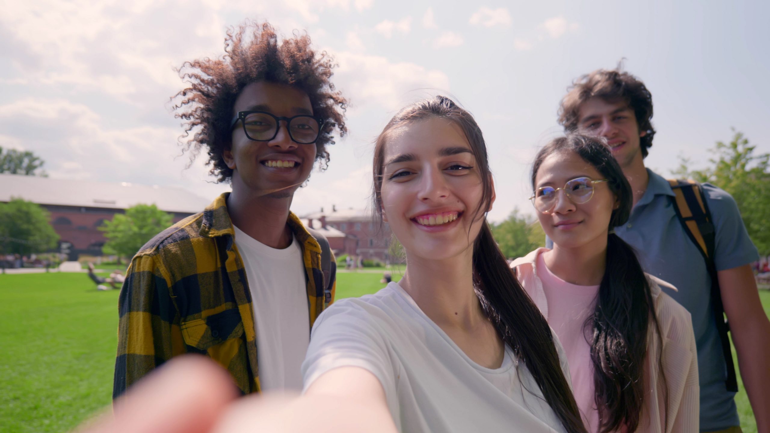 Pov shot of multiethnic young friends having video call or taking selfie together in park. Diverse young people looking at camera and talking standing outdoors