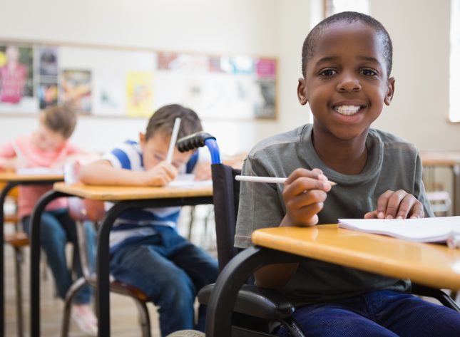 Child with a wheelchair smiling at camera in classroom