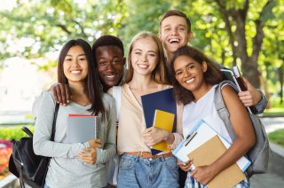 Group of diverse happy students with books and notebooks having fun in park after studying, smiling at camera