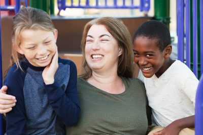 Laughing mother embracing two giggling young sons at park outside