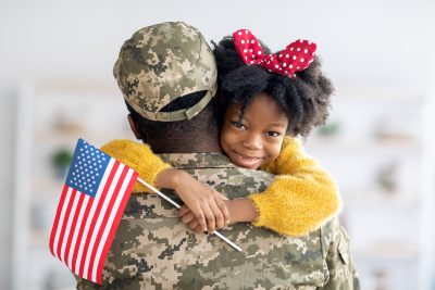 Cute Little Black Girl Holding American Flag And Embracing Soldier Dad, Happy Female Child Hugging Father In Military Uniform, Welcoming Home After Turning Back From US Army, Closeup Shot