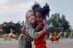 Diverse happy kids hugging on children playground. Portrait of adorable preschool african and caucasian girls embracing and smiling outdoors in park