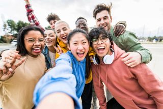 Diverse friends taking big group selfie shot smiling at camera -Laughing young people standing outdoor and having fun - Cheerful students portrait outside school