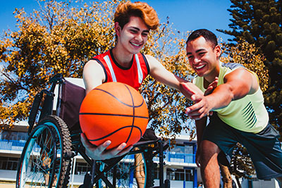 Latin young man using wheelchair and playing basketball with a friend