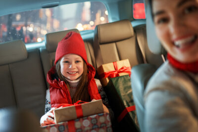 Woman and her child holding presents and delivering them on car to home. Holidays concept. Time of Christmas Eve.