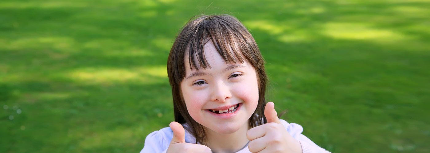 Child with Down Syndrome smiles and gives two thumbs up