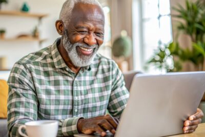 Older Black man smiling and looking at laptop