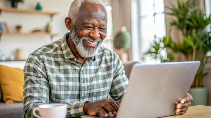 Older Black man smiling and looking at laptop