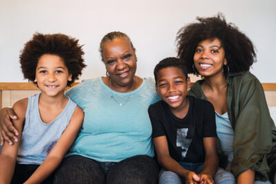 Portrait of African American grandmother, mother and children looking at camera and smiling while sitting on sofa at home. Kinship Family and lifestyle concept.