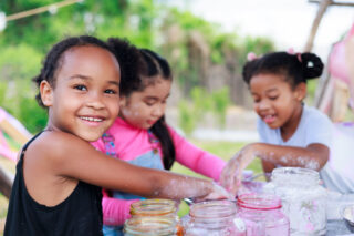 Lovely Asian and smiling African girls making and play colorful dough together at playground, summer camp learning