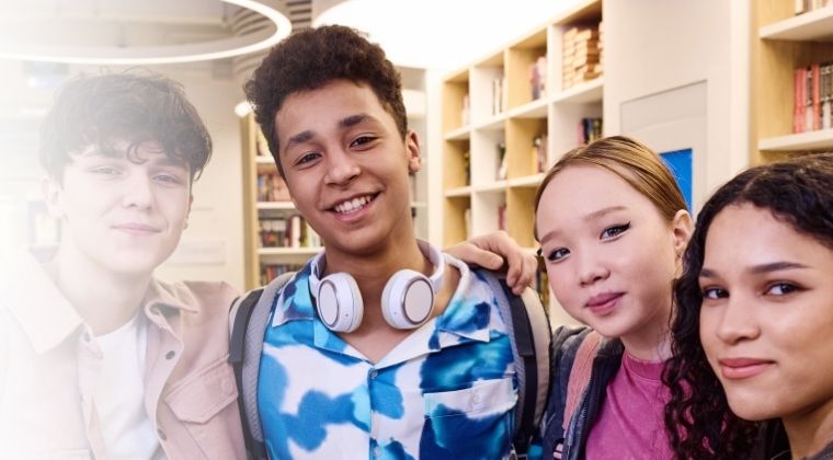 POV selfie photo of multiethnic group of students smiling at camera in school library
