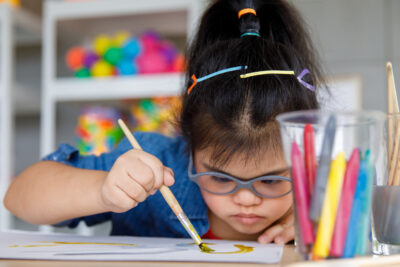 Young Asian down syndrome little girl sitting at desk with colors and painting with concentrated and calm. painting. Concept for special education