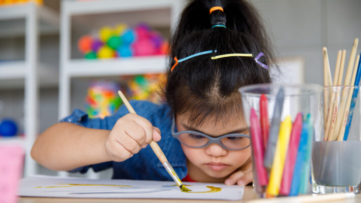 Young Asian down syndrome little girl sitting at desk with colors and painting with concentrated and calm. painting. Concept for special education
