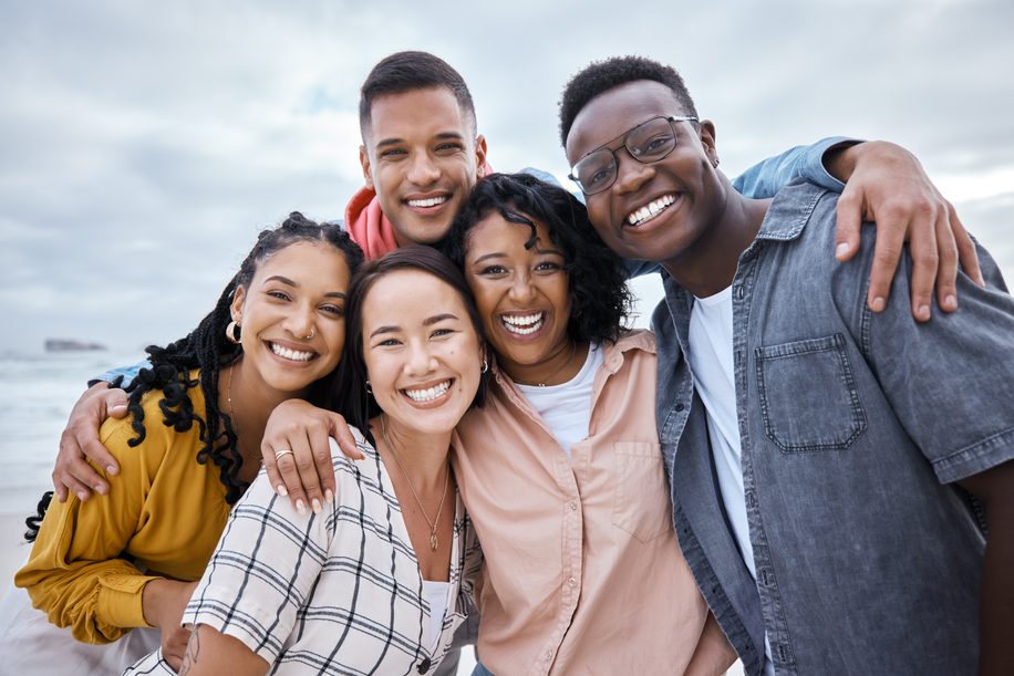 Friends, diversity and portrait at beach, ocean and outdoor nature for fun, happiness and travel. Group of happy young people at sea for holiday, vacation and smile for relaxing weekend trip together.